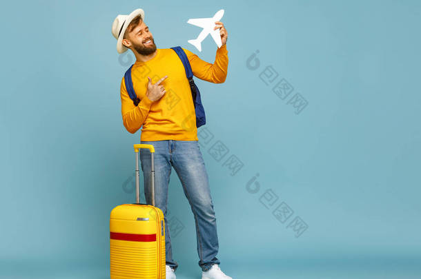 全身上下喜怒无常的男人笑着指着玩具飞机，站在蓝色背景的行李旁边