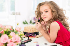 一个小女孩用化妆品。她是在母亲的卧室里，坐在靠近镜子.