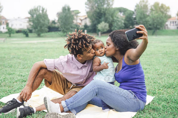 快乐的非洲家庭在一个公共公园户外用手机摄像头<strong>自拍自拍</strong>--爸爸妈妈在周末阳光明媚的日子里和女儿<strong>一起</strong>玩--爱情和幸福的概念
