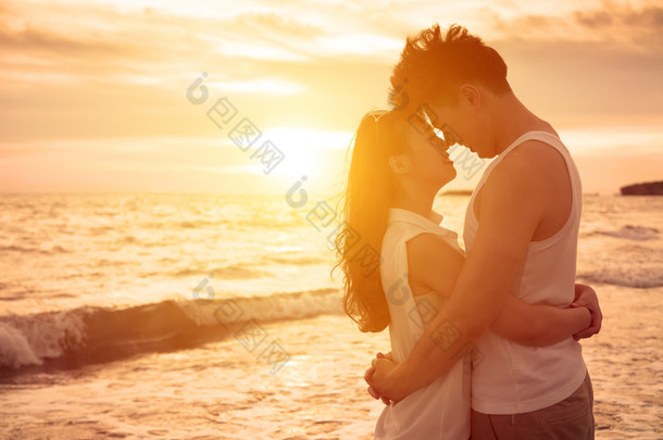年轻的夫妇在海滩上在日落时接吻