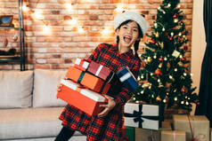 可爱的女孩拿着礼物显示大露齿微笑。可爱的女儿, 圣诞老人的帽子站在圣诞树前。在圣诞节快乐地得到礼物在家里.