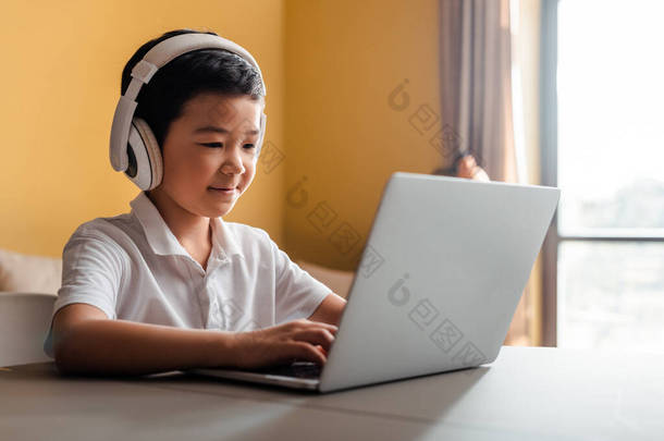 在检疫期间，带着<strong>笔记本电脑</strong>和耳机在网上学习的亚洲男孩笑了
