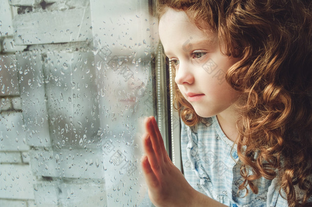 Sad child looking out the window. Toning photo.