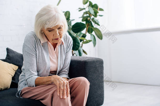 老年妇女膝关节关节炎，<strong>坐</strong>在公寓<strong>沙发上</strong> 