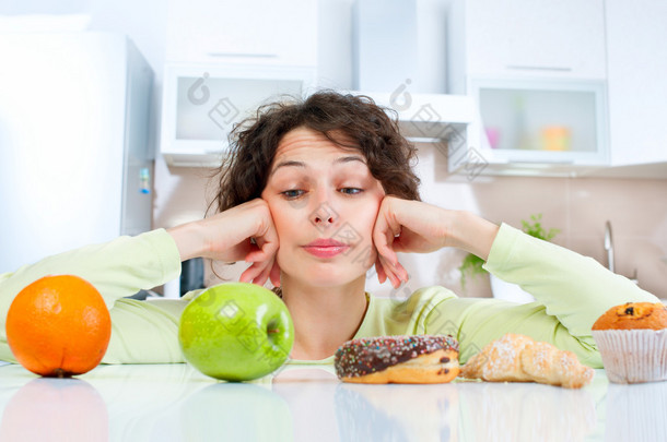 节食的概念。在<strong>水果</strong>和糖果之间做出选择的年轻女子