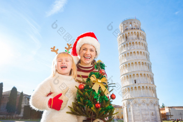 Happy woman and baby girl holding Christmas tree. Pisa, Italy