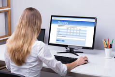 在计算机上填写在线调查表的女实业家的后视图
