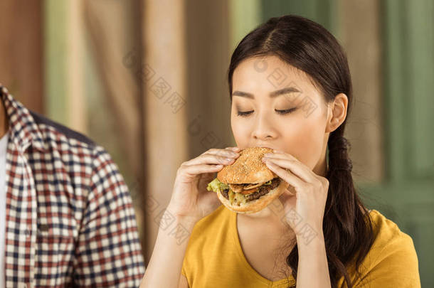 年轻的亚洲女孩吃汉堡