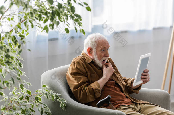 老年人坐在扶手椅上用数码平板电脑震惊了
