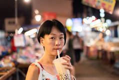 亚洲女人在夜市端着著名的泰国泡泡奶茶