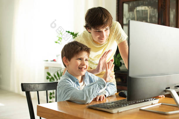 微笑的男孩和青少年在<strong>网上</strong>聊天，在电脑屏幕上挥手。由于头孢病毒而产生的隔离和自我隔离。COVID-19