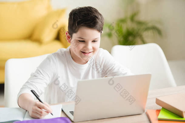 <strong>开朗</strong>的男孩使用笔记本电脑和写在抄本，而在家里做功课