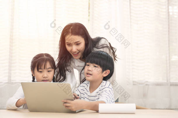 有孩子的快乐的亚洲家庭和他们的妈妈用电脑在家里做作业.