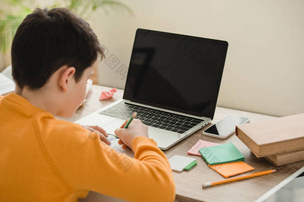 小学生做家庭作业，而坐在办公桌<strong>附近的</strong>笔记本电脑与空白屏幕