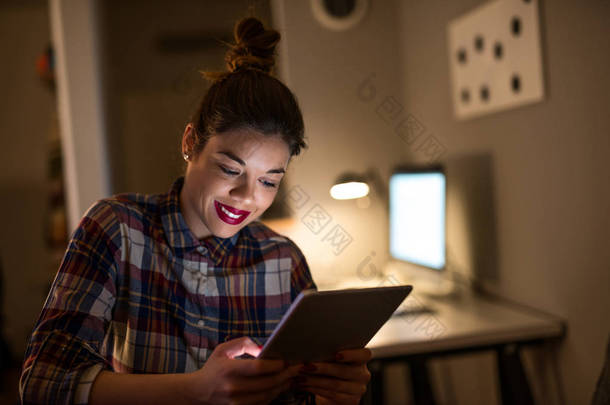 关闭了年轻的女商人在平板电脑上数字工作到深夜的肖像.