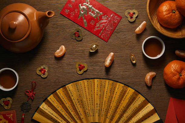 木桌<strong>上新</strong>鲜成熟的橘子、茶具、带象形文字和金币的扇子的顶部视图 