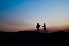 年轻的男人和女人在夕阳下一起奔跑。剪影