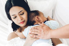 母亲和父亲抱着婴儿在她的怀里, 在一个白色的卧室。对家庭概念的爱