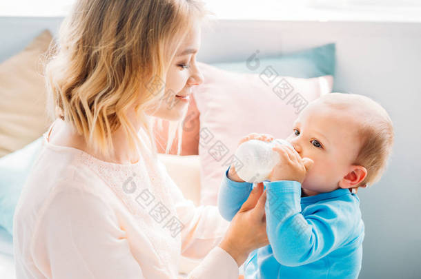 快乐的母亲在家喂养她的孩子与<strong>婴儿奶瓶</strong>