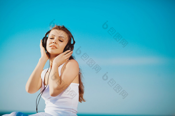 美丽的女人，听听音乐耳机在海边蓝天的衬托