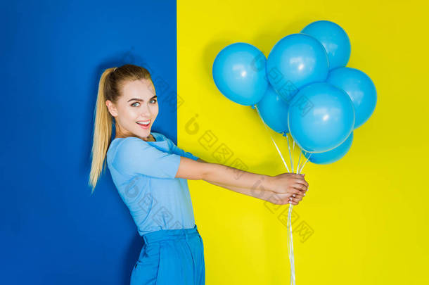 有吸引力的年轻女孩拿着蓝气球在<strong>蓝色</strong>和<strong>黄色背景</strong>一束