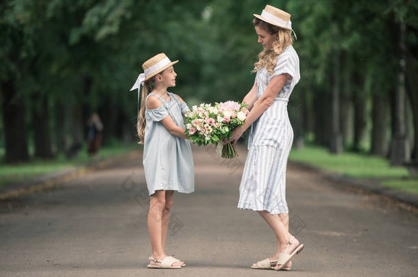 妈妈和女儿在公园里捧着鲜花花束的草帽