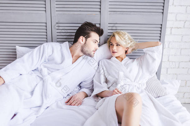 美丽的<strong>年轻</strong>夫妇在浴袍看着对方, 而躺在一起在床上