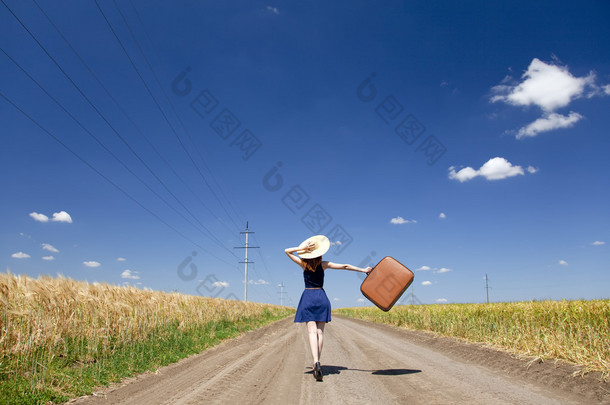 孤单的小女孩带着手提箱在乡村道路.