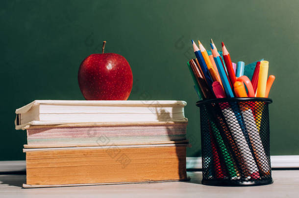 书和笔架上的成熟苹果，书桌上有彩色铅笔和毛笔，靠近绿色黑板