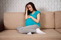 怀孕妇女的抑郁症。一个年轻的孕妇坐在沙发上哭着回家.