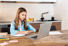 在家里进行电子学习的同时，有选择地关注可爱的孩子在笔记本电脑旁写作的问题