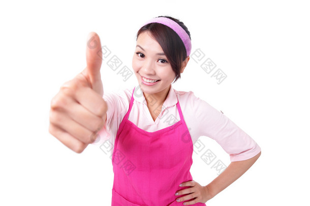 幸福的年轻女人的家庭主妇穿厨房围裙和显示竖起大拇指