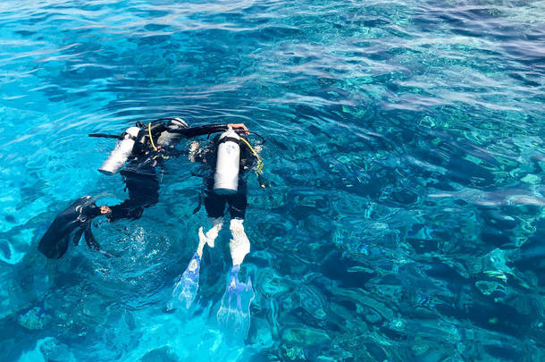 两名潜水员在黑色潜水衣, 一个男人和一个女人与氧气瓶下沉在透明的蓝色水的海洋, 海洋在一个热带天堂温暖的<strong>度假胜地</strong>.