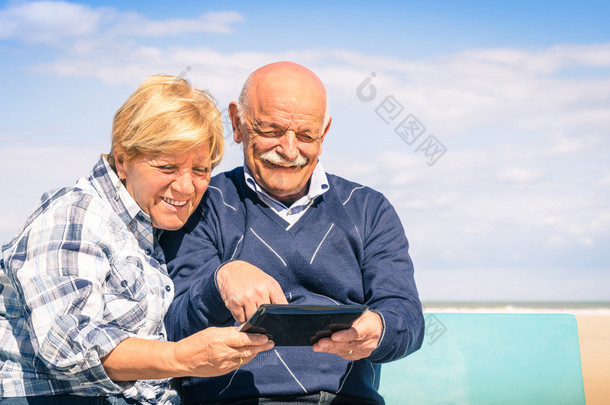 高级幸福的夫妇在海滩-肖像的男人和女人与现代科技互动玩一款平板电脑