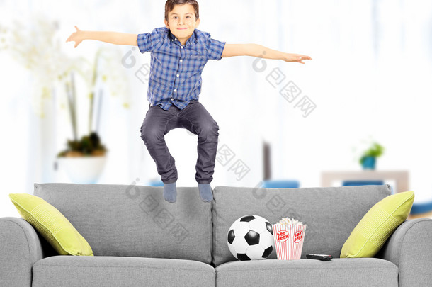 喜出望外的男孩跳上在家里的沙发上 