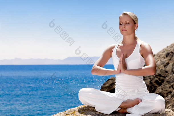 服装在白坐在海边岩石上的漂亮女孩