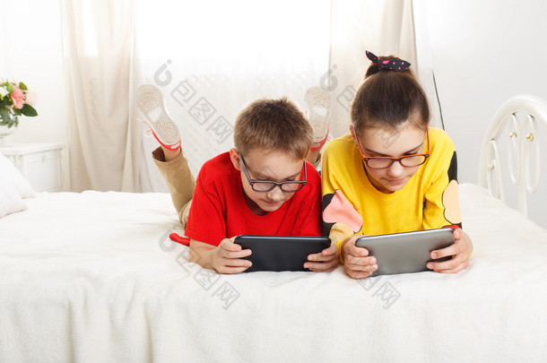 两个孩子玩在平板电脑躺在床上