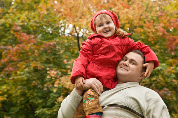 小女孩坐在公园的男人的肩膀在秋天