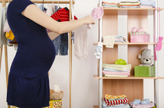 怀孕的女人逛街买衣服，她刚出生的婴儿。安排在 hangers.colorful 衣柜的新生儿的衣服更衣衣橱，孩子们，充满了所有的衣服、 鞋子、 配件和玩具的婴儿
