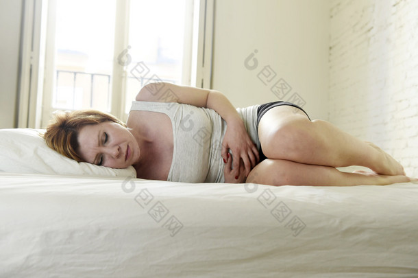 young beautiful woman suffering stomach cramps on belly holding tummy with her hands in period pain