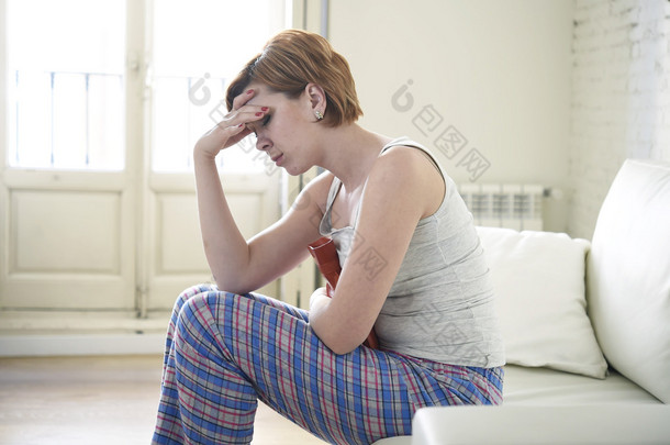 young woman holding hot water bottle in belly suffering stomach cramp and period pain 