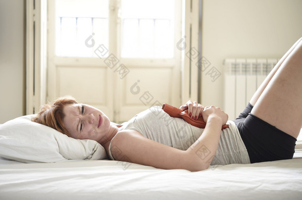 young woman suffering stomach cramps on belly holding hot water bottle against tummy