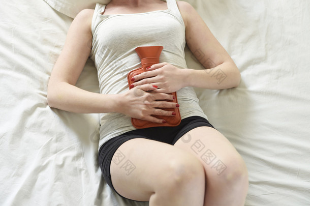 young woman suffering stomach cramps on belly holding hot water bottle against tummy