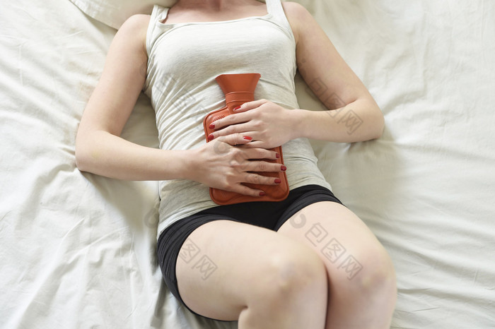 young woman suffering stomach cramps on belly holding hot water bottle against tummy