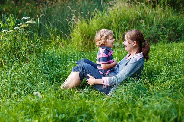 小男孩和他的母亲坐在草在夏季森林