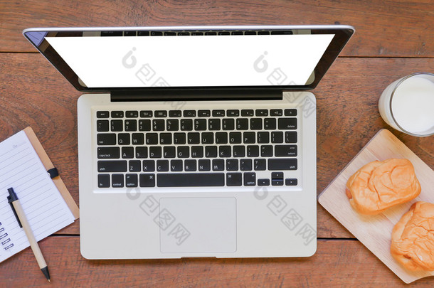 笔记本手提电脑、 面包和木桌背景上的牛奶杯.