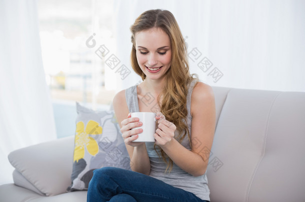 年轻的女人坐在沙发上抱着杯子的内容