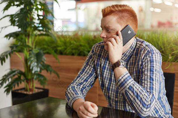 有吸引力的红发男人水平肖像穿着优雅的衬衫，坐在餐厅里，在绿色的背景，与他的女朋友一边望著远方通信移动电话
