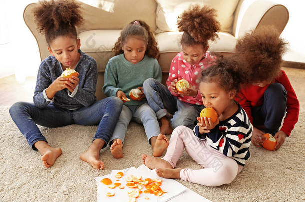 五可爱的非洲女孩坐在地板上, 吃橘子