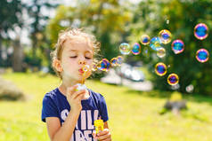 一个小女孩在夏天公园吹肥皂泡泡。背景色调 instagram 筛选器.